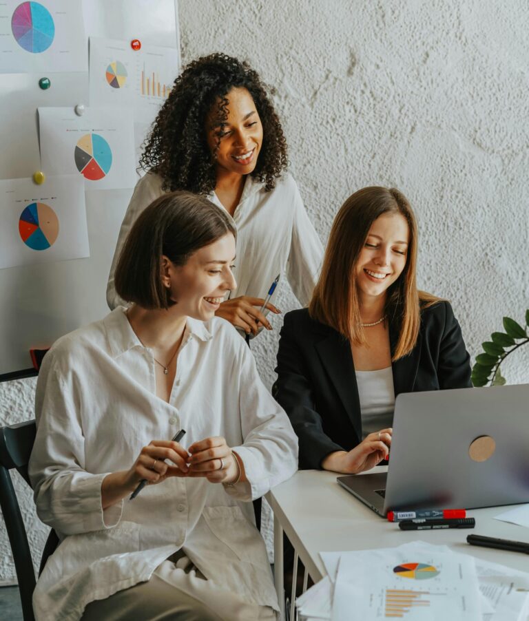 Three businesswomen collaborate with graphs and a laptop in a modern office setting.